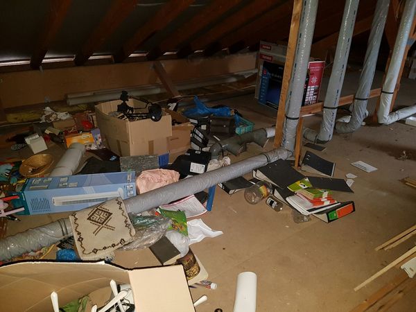 Dachboden mit Rohren, Kartons, Büchern und verschiedenen Gegenständen im Chaos.