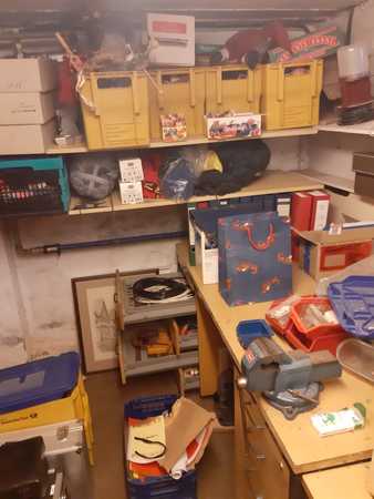 Ein vollgestellter Kellerraum mit Regalen, Werkzeugen und verschiedenen Aufbewahrungsboxen.