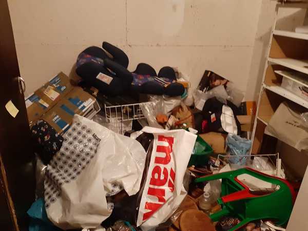 Unordentlicher Abstellraum mit Kartons, Plastiktüten, Regalen und diversen Haushaltsgegenständen.